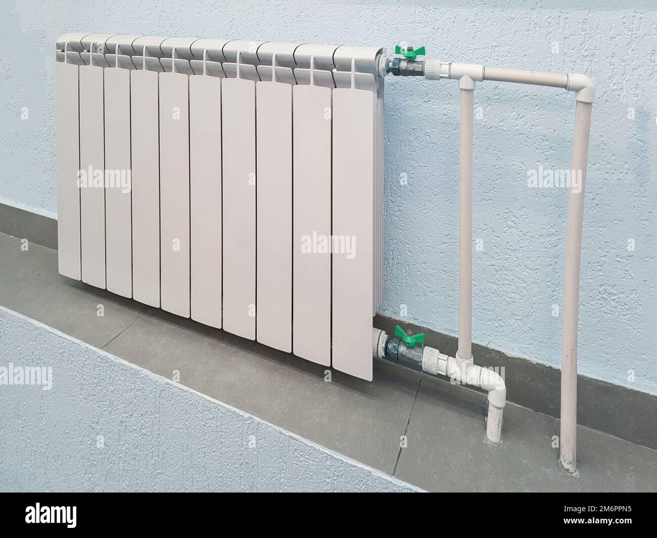 Moderna batteria bianca in alluminio per il riscaldamento dell'acqua calda, sullo sfondo di una parete all'interno di un appartamento o fuori Foto Stock