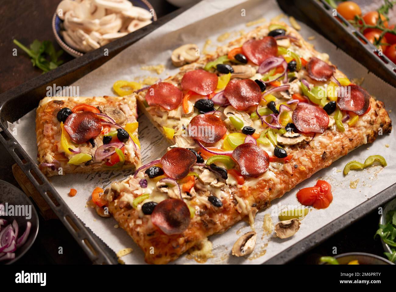 Un pezzo di pizza quadrata con pomodori peperoni al basilico e funghi su un vassoio di ferro Foto Stock