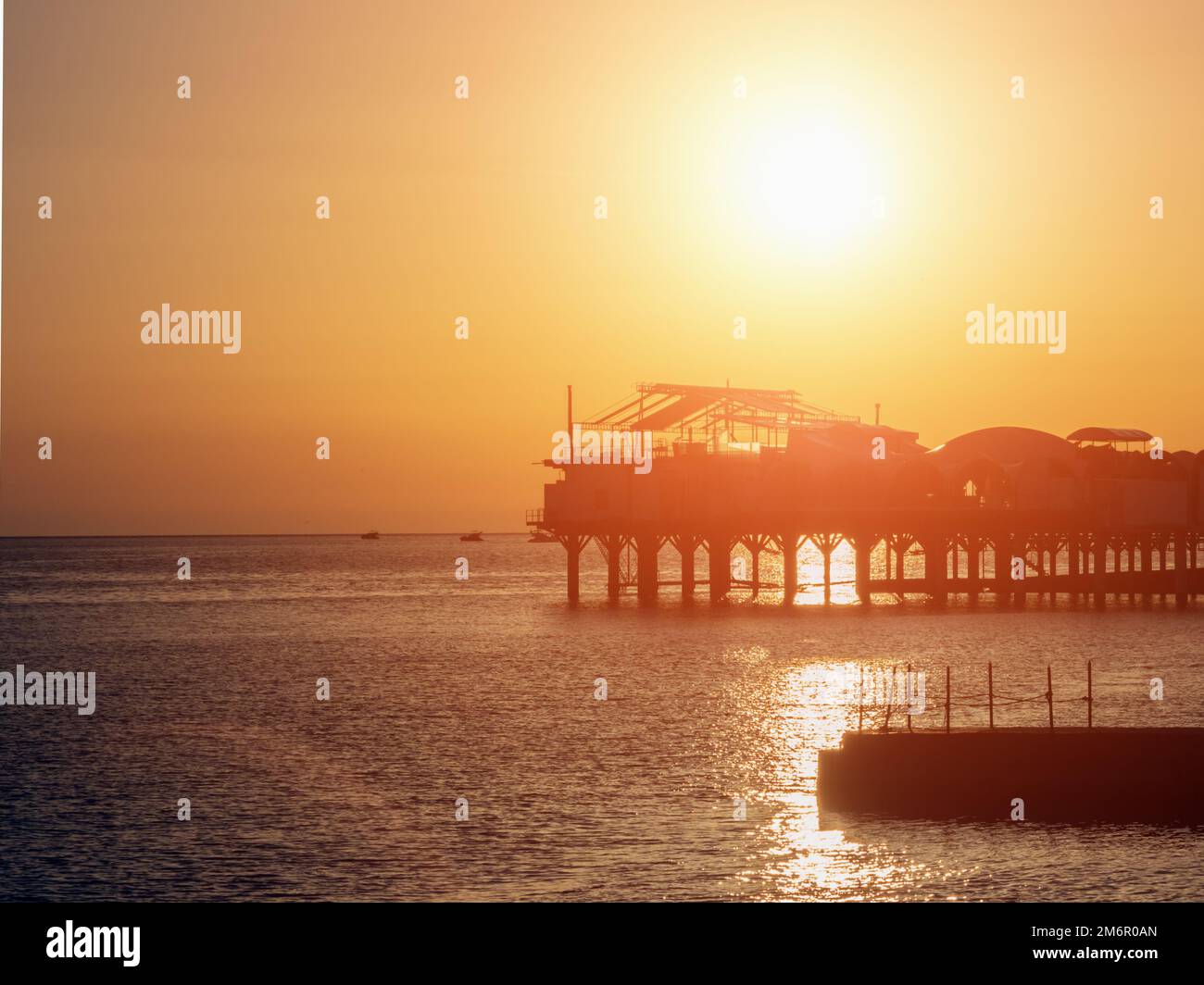 Silhouette di un edificio su un molo in un mare calmo al tramonto. Costruzione sul molo in mare al tramonto. Caffè sul molo a s Foto Stock