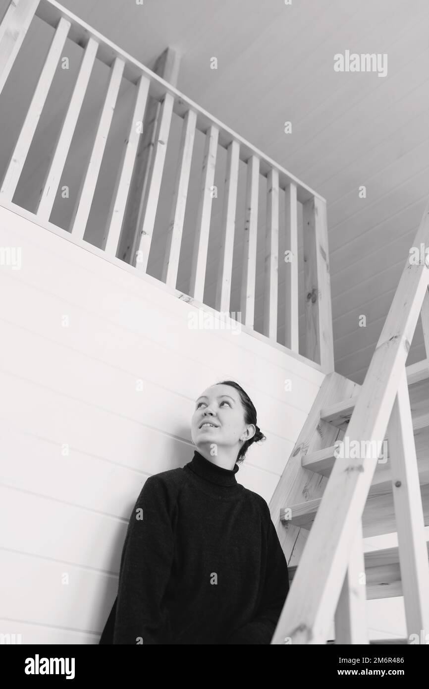 Giovane donna seduta su scale di legno in casa moderna. Bella brunetta a casa. Casa accogliente Foto Stock