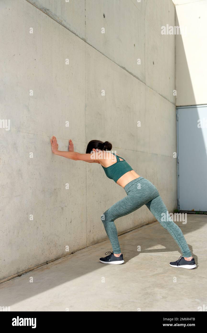 donna che fa un polpaccio o gamba si allunga contro una parete di cemento  all'esterno, esercizi di riscaldamento Foto stock - Alamy