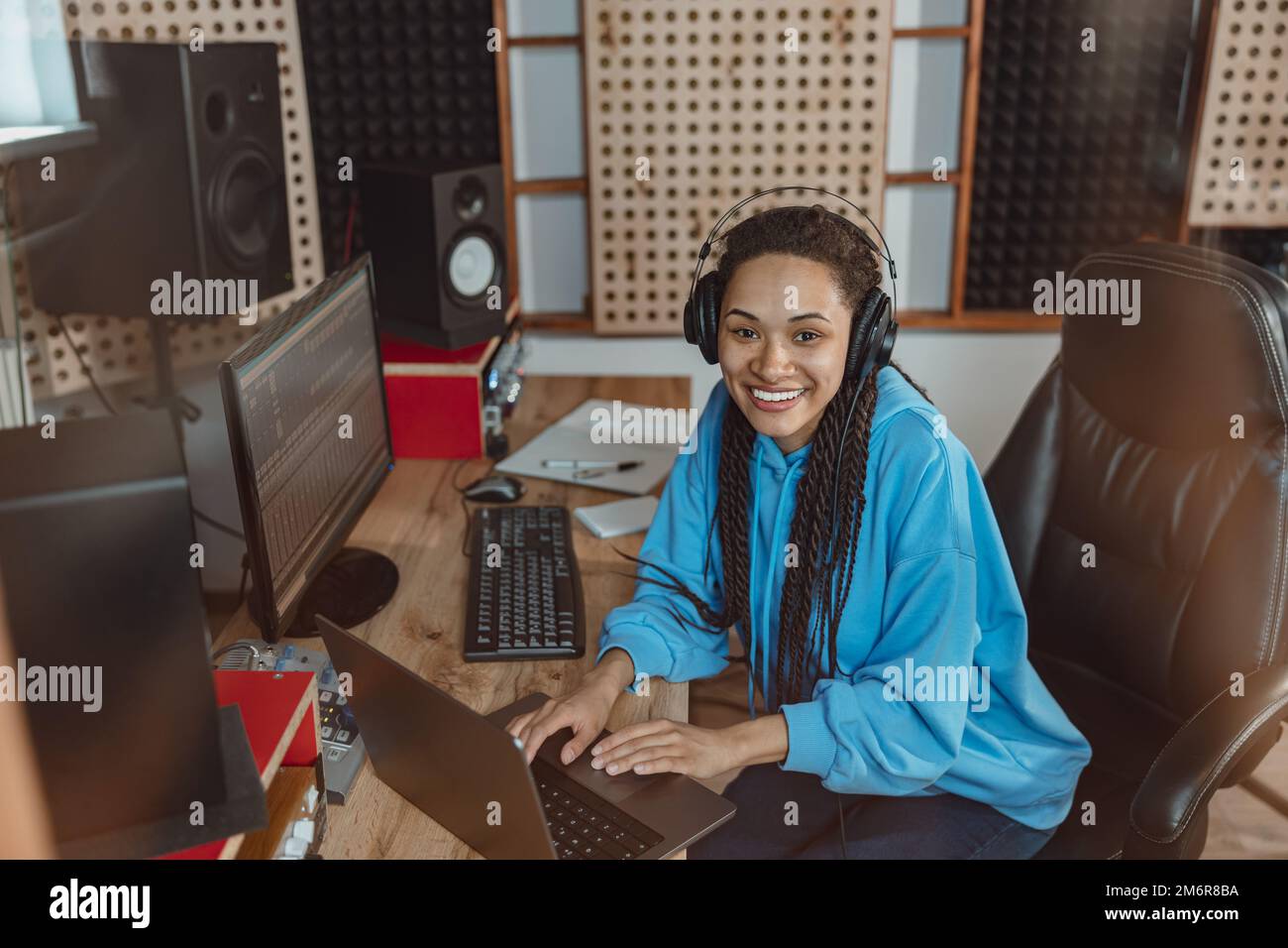 Bella donna ingegnere del suono, presentatore radio, sorride alla fotocamera mentre lavora su un computer portatile in studio di trasmissione Foto Stock