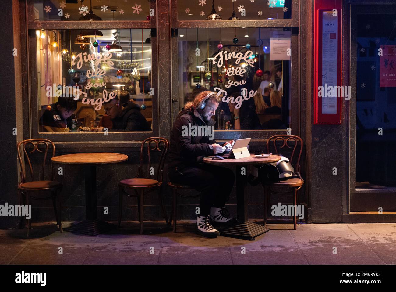 L'uomo sedette fuori dal ristorante Balans sul suo computer portatile, Old Compton Street, Soho di notte, in vista di Natale 2022, Londra, Inghilterra, Regno Unito Foto Stock