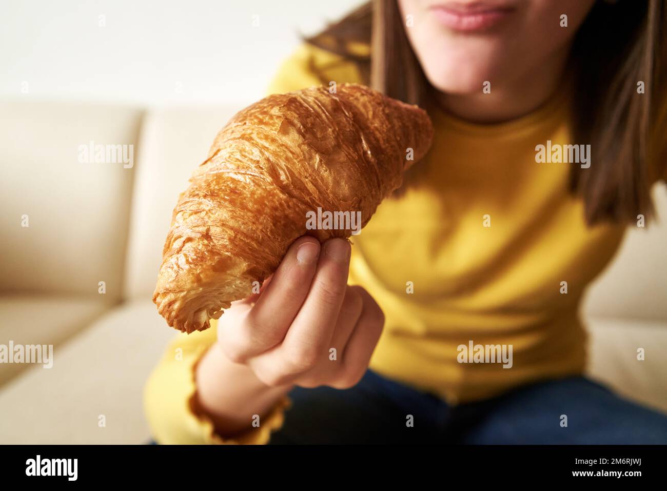 Croissant - dolce in mano ad una ragazza adolescente che fa colazione, primo piano Foto Stock