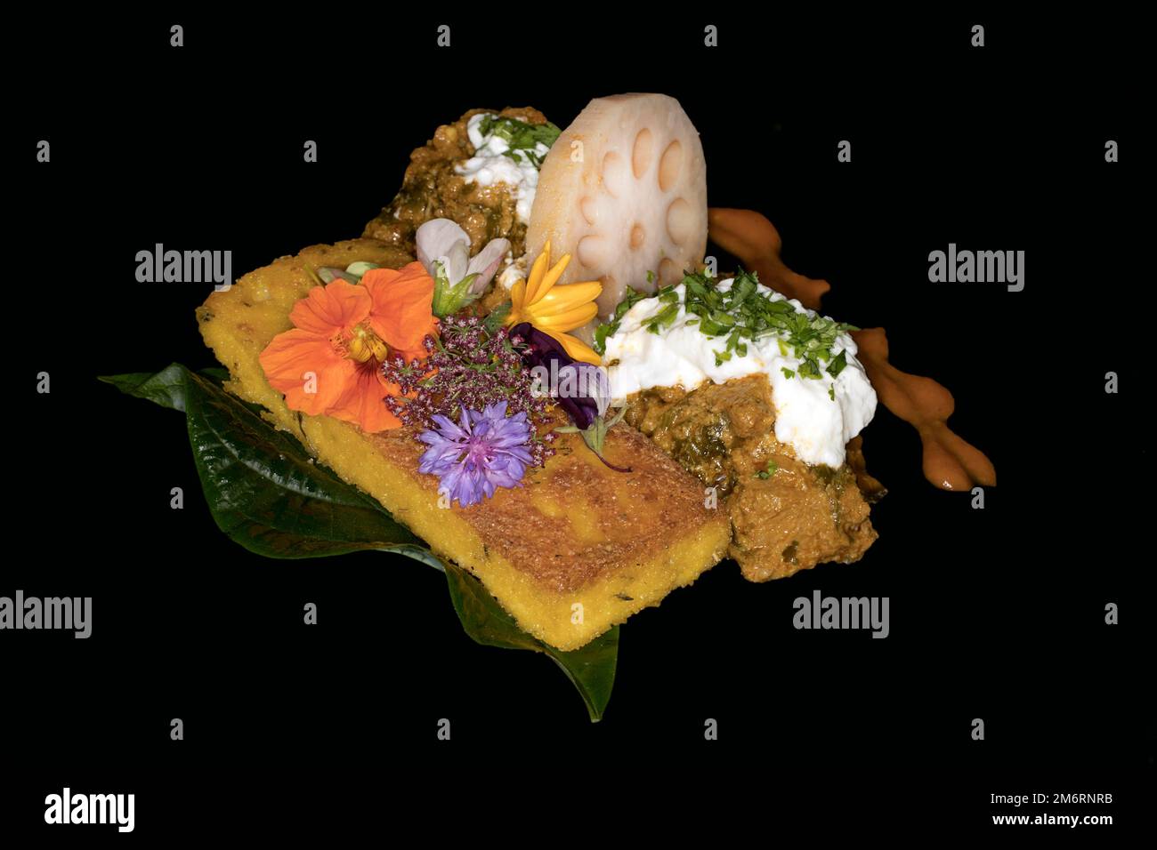 Korma al curry indiano, con yogurt, fetta di polenta fritta, fetta di radice di loto e fiori di prato come decorazione su una foglia di avocado, fotografia con Foto Stock