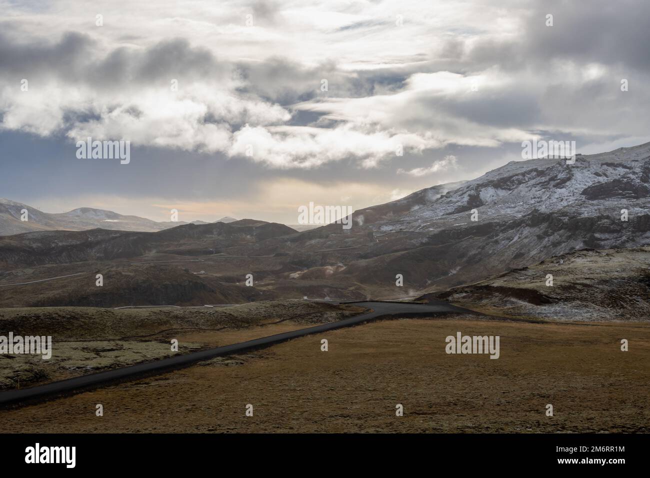 Terreno coperto da lichene ed erba. Grandi montagne sullo sfondo, coperte dalla prima neve autunnale. Nuova strada che attraversa la valle. Sk nuvoloso intenso Foto Stock