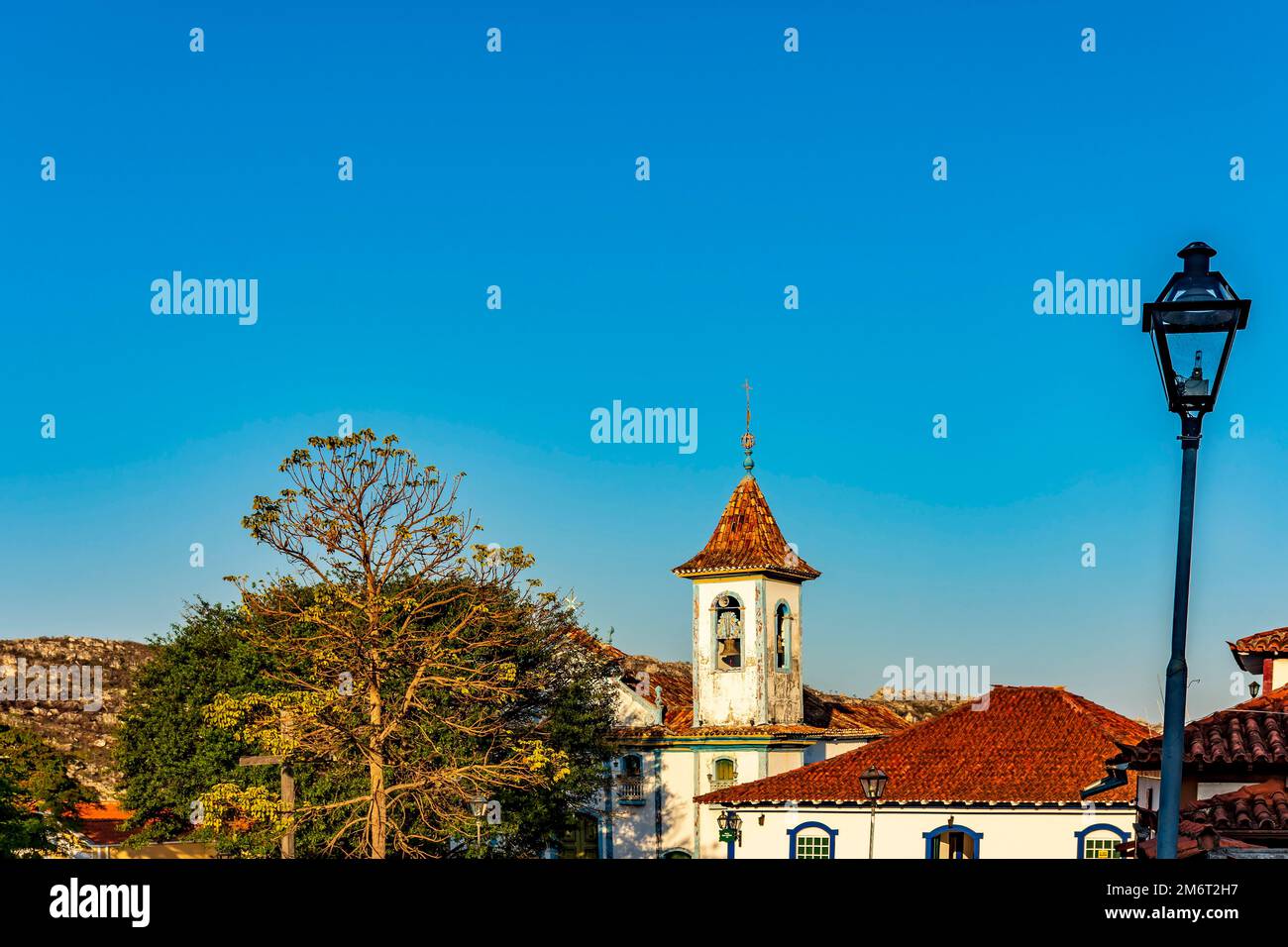 Torre della chiesa barocca con campana che si innalza attraverso gli alberi e i tetti Foto Stock