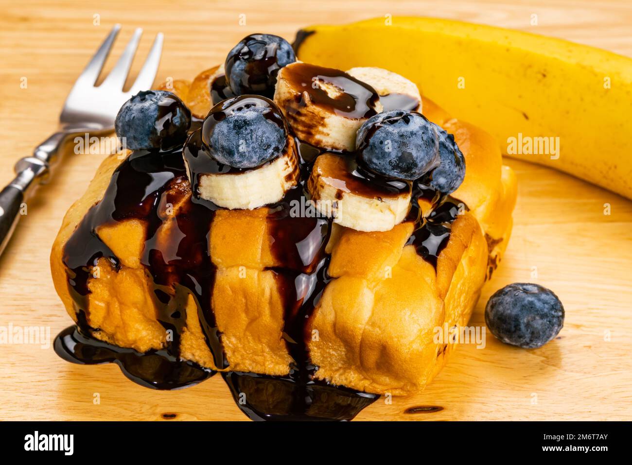 Vista ad angolo alto della guarnizione del pane con banana a fette e mirtillo versato con sciroppo al cioccolato. Foto Stock