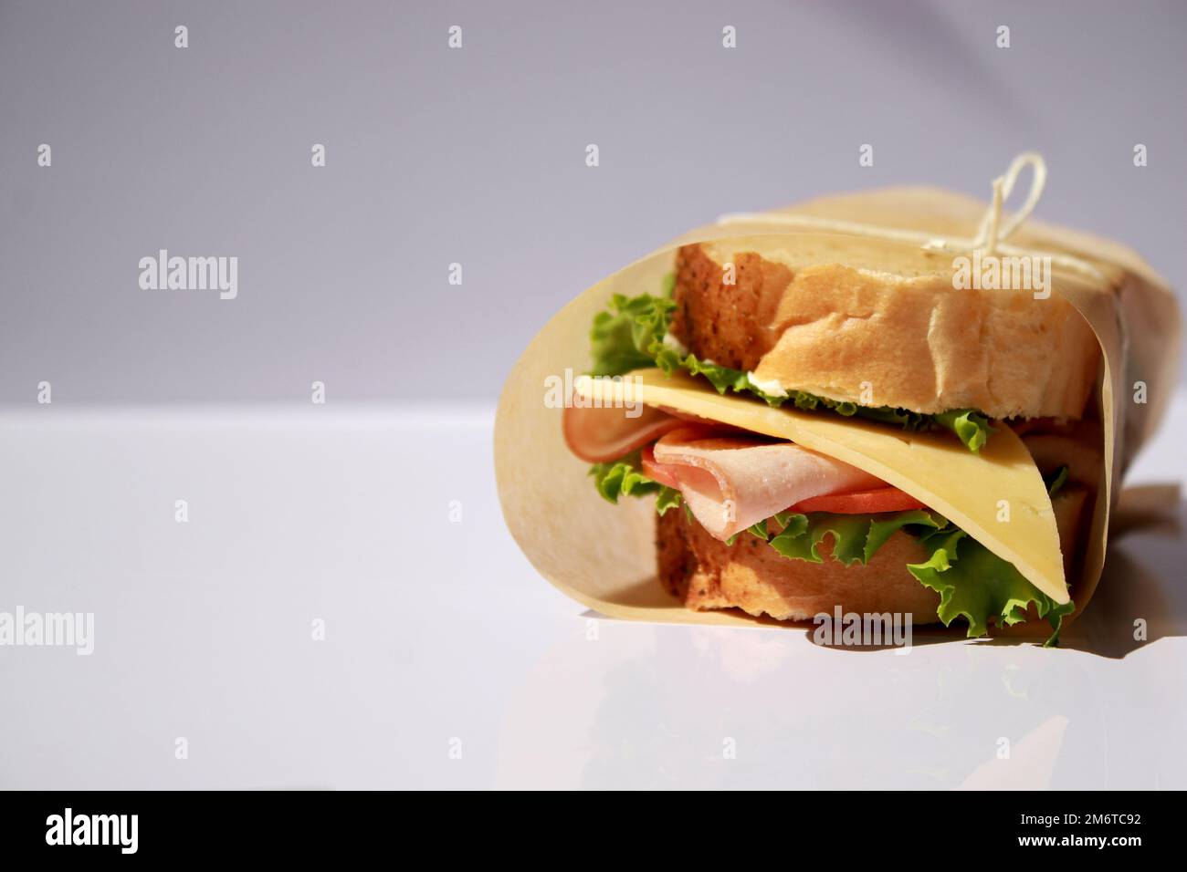 Panino di formaggio e prosciutto avvolto in carta su sfondo bianco con spazio copia Foto Stock