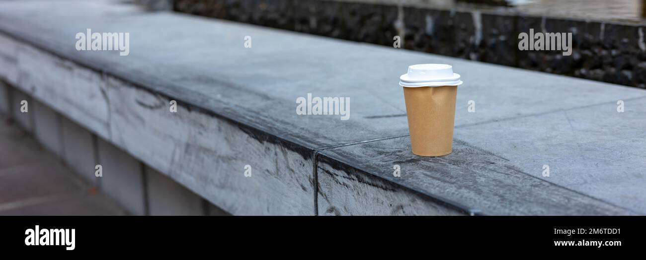 banner o usato usa e getta tazza di carta abbandonata su banco di cemento in strada città Foto Stock