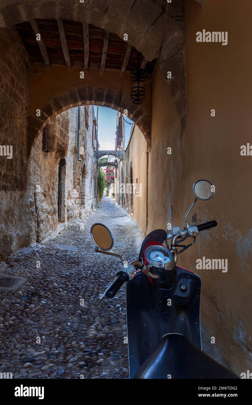 Strette strade acciottolate storiche di Rodi. Scooter moto d'epoca è parcheggiata vecchia pietra contro il muro di casa, Rodi, Dodecaneso, Grecia Foto Stock