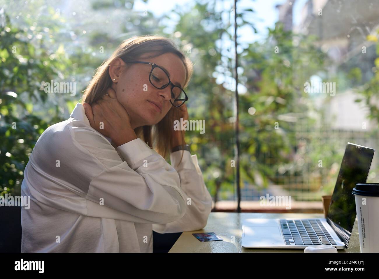 Donna stressata stanca che soffre di dolore alla nuca lavorando da casa ufficio seduto a tavolo. Donna giovane anziana iperlavorata massaggiando il collo sensazione di dolore ferito Foto Stock