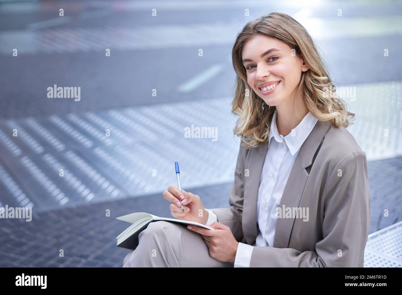 Donna in tuta si siede nel centro della città, scrive, prende appunti, tiene la penna e il notebook, brainstorms, crea idee Foto Stock