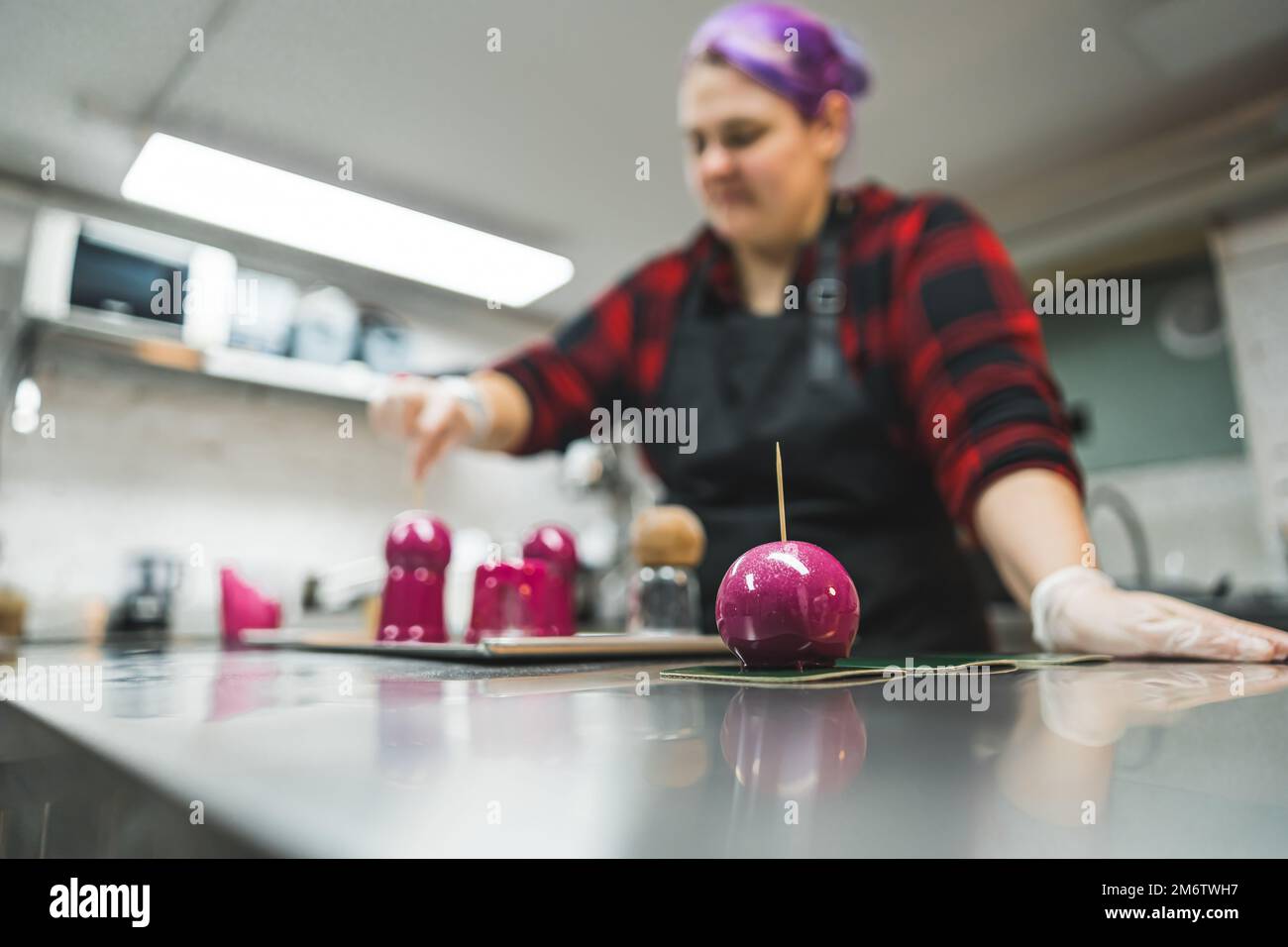 Interno cucina pasticceria chef. Processo di decorazione. Donna caucasica che ricopre cupcakes e praline in glassa rosa. Foto di alta qualità Foto Stock