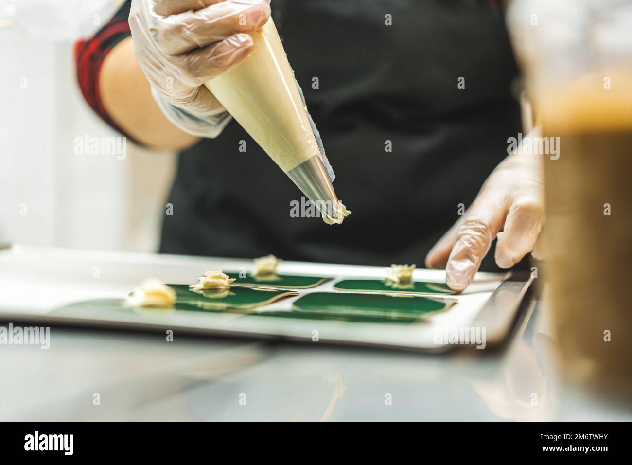 La crema bianca viene applicata su un piatto verde con l'uso di un sacchetto per pasticceria da parte di un panettiere. Primo piano sfocato. Foto di alta qualità. Foto Stock
