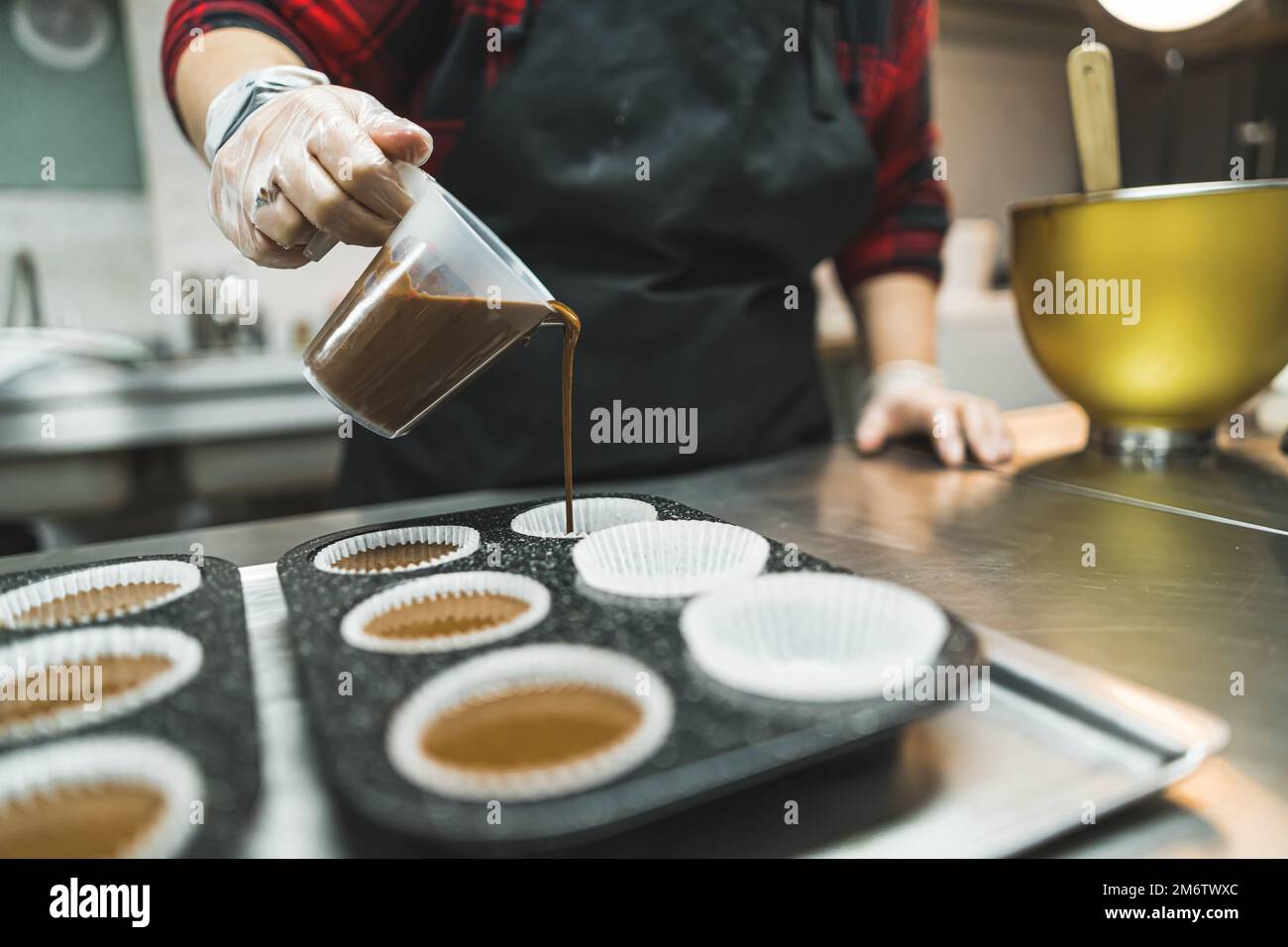 Pastella cupcake al cioccolato. Inriconoscibile pasticciere caucasico versare pastella in carta muffa muffin in liner muffin. Foto di alta qualità Foto Stock
