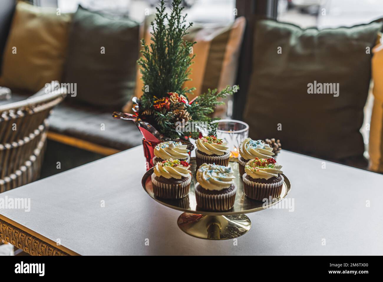 Caffè interno con prodotti da forno. Stand d'oro posto sul tavolo con adorabili cupcake con gelato alla vaniglia e spruzzate colorate. Natale. Foto di alta qualità Foto Stock