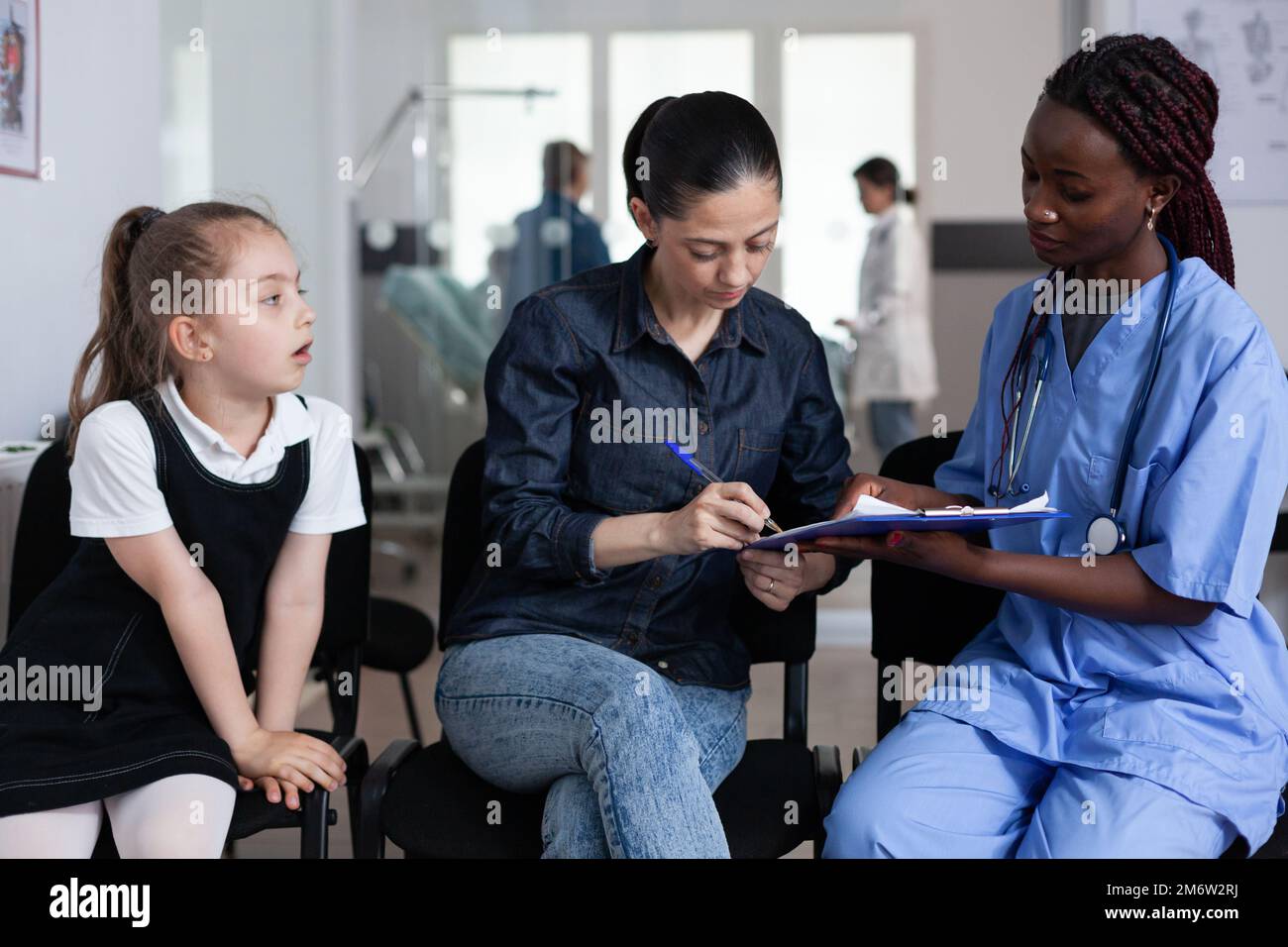 Dottore afroamericano che compila la documentazione di ammissione dei bambini all'ospedale pediatrico. Giovane donna ospedalizzante figlia malata in clinica medica. Infermiera che frequenta la madre, bambina nella lobby del sanatorio. Foto Stock