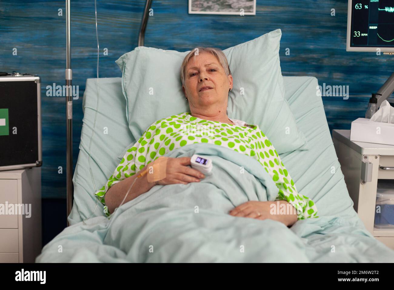 Donna anziana sdraiata nel letto di ospedale mentre i segni vitali e i livelli di ossigeno nel sangue sono presi. Paziente anziano malato cronico in trattamento in un centro sanitario specializzato. Foto Stock