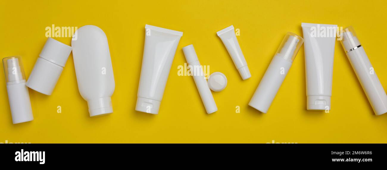 Vari tipi di confezioni di plastica bianca: Una bottiglia, un vasetto, un tubo su fondo giallo. Contenitore per cosmetici Foto Stock