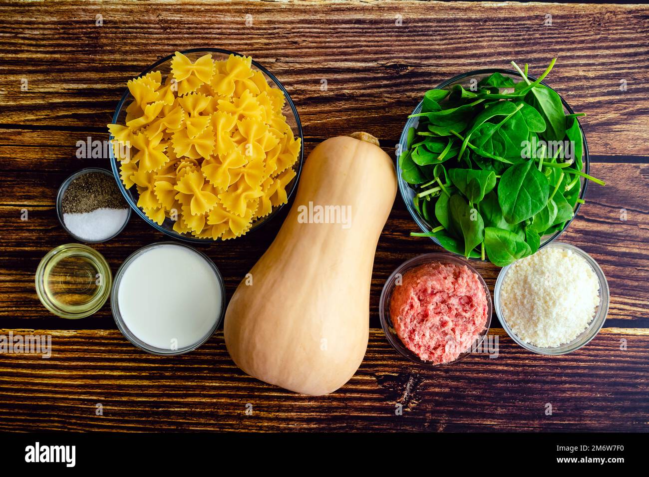 Cremoso arrosto di zucca Squash Pasta con salsiccia e spinaci ingredienti: FARFALLE pasta, zucca invernale, e altri ingredienti crudi su un tavolo di legno Foto Stock