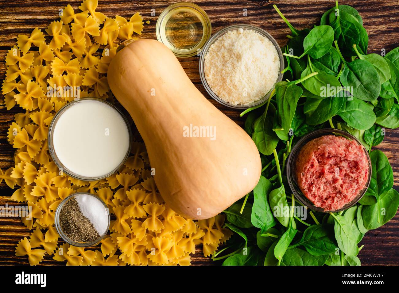 Cremoso arrosto di zucca Squash Pasta con salsiccia e spinaci ingredienti: FARFALLE pasta, zucca invernale, e altri ingredienti crudi su un tavolo di legno Foto Stock