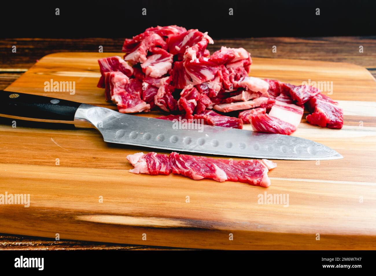 Bistecca di Ribeye a fette sottili su un tagliere di legno con un coltello: Strisce di manzo a fette sottili con un coltello di santoku su un tagliere di legno Foto Stock