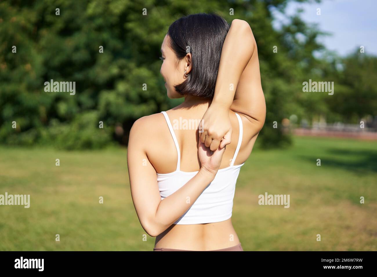 Vista posteriore della giovane donna sportiva che si stende le braccia dietro la schiena, riscaldamento, preparazione per il jogging allenamento, evento sportivo nel parco Foto Stock