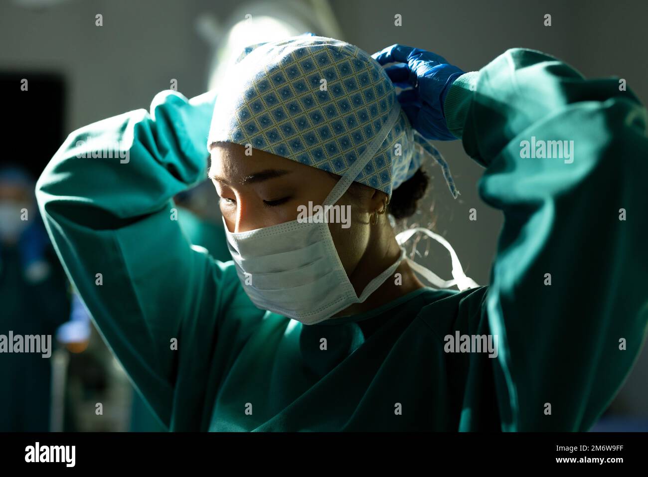 Chirurgo asiatico femminile in cappuccio chirurgico e maschera di legatura abito in teatro operatorio Foto Stock