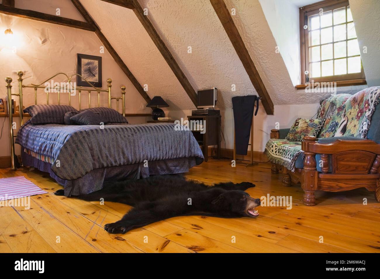 Tappeto con orso nero e letto queen size in ottone nella camera da letto principale al piano superiore all'interno di una casa in legno ricostruita nel 1980. Foto Stock