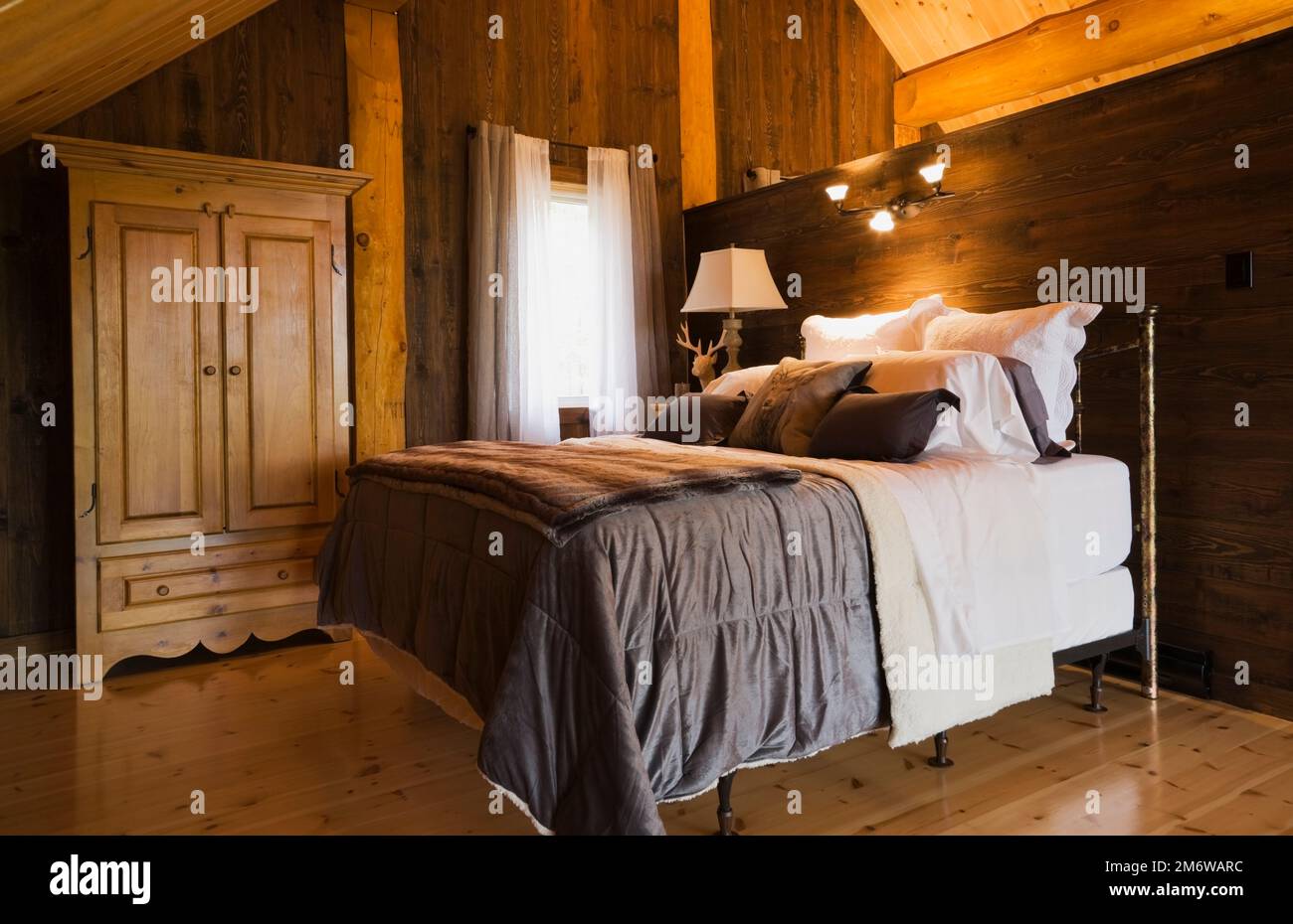 Letto queen size con copriletto marrone e comodino nella camera da letto principale sul mezzanino all'interno di una lussuosa casa in legno in stile cottage. Foto Stock