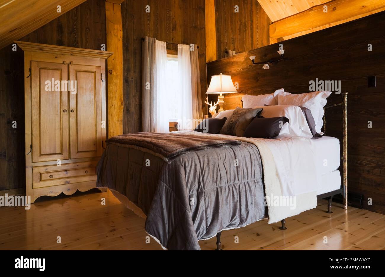 Letto queen size con copriletto e guardaroba marrone nella camera da letto principale sul mezzanino all'interno di una lussuosa casa in legno in stile cottage. Foto Stock