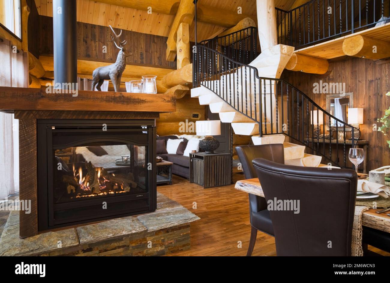 Tavolo da pranzo in legno, sedie in pelle marrone nella sala da pranzo, caminetto a gas e scale in legno sbiancate con ringhiera in ferro battuto nero nel soggiorno. Foto Stock
