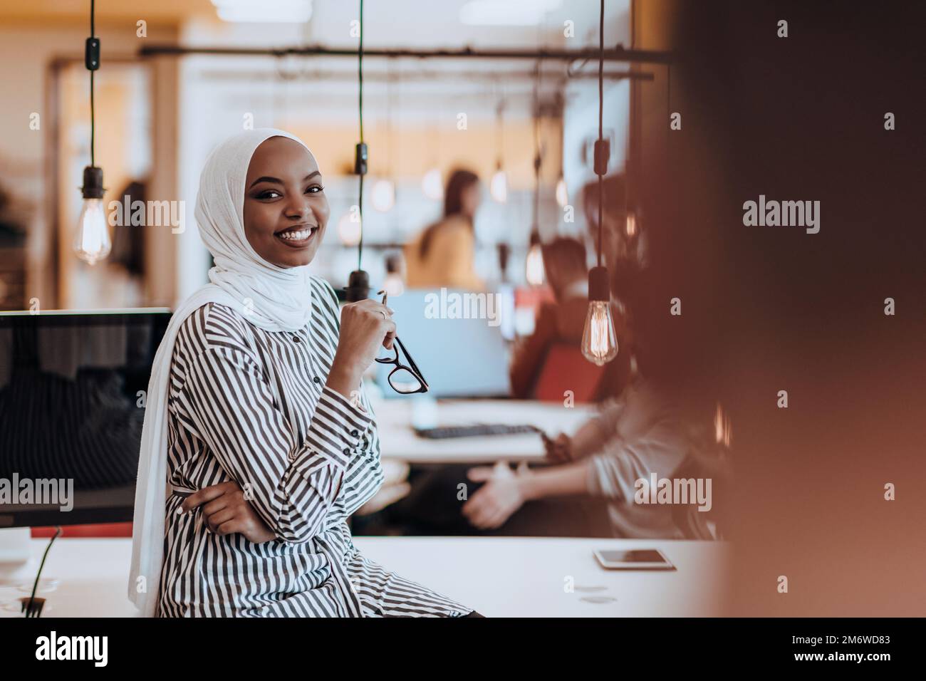 Protarit di una donna musulmana nera (afro-americana) in piedi in un moderno ufficio d'affari mentre indossa un hijab. Foto Stock