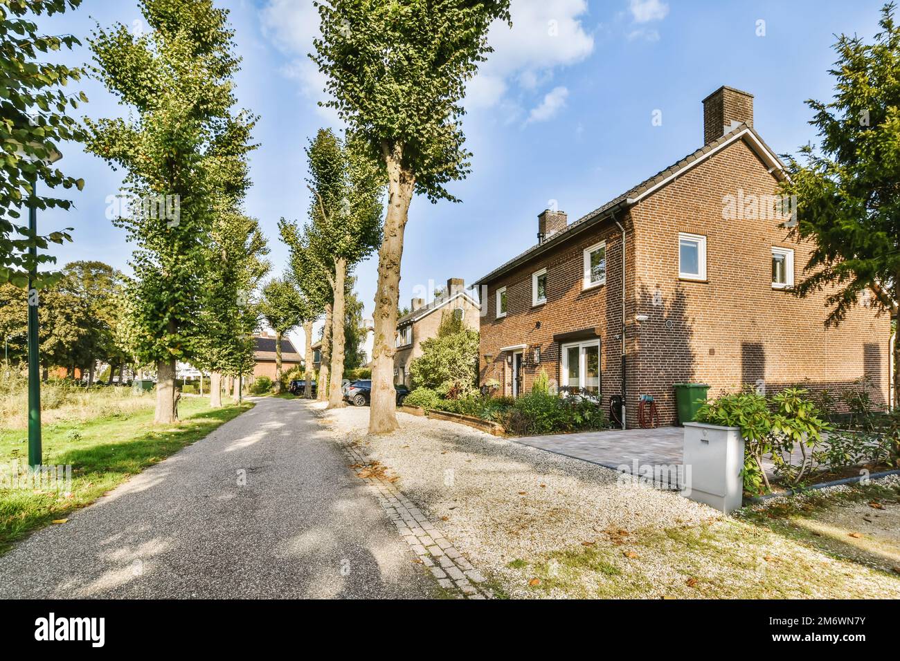 una casa in mattoni con alberi nel cortile anteriore e cielo blu sopra, scattata in una foto di scorta di giorno di sole estate Foto Stock
