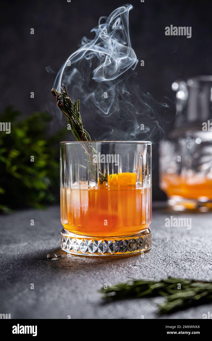 Negroni con rosmarino fumante. Negroni con ghiaccio e arancio su sfondo scuro. Cocktail Negroni in un bicchiere con rosema fumante Foto Stock