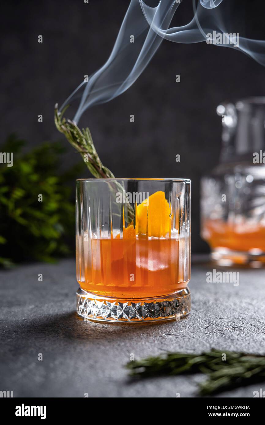 Negroni con rosmarino fumante. Negroni con ghiaccio e arancio su sfondo scuro. Cocktail Negroni in un bicchiere con rosema fumante Foto Stock