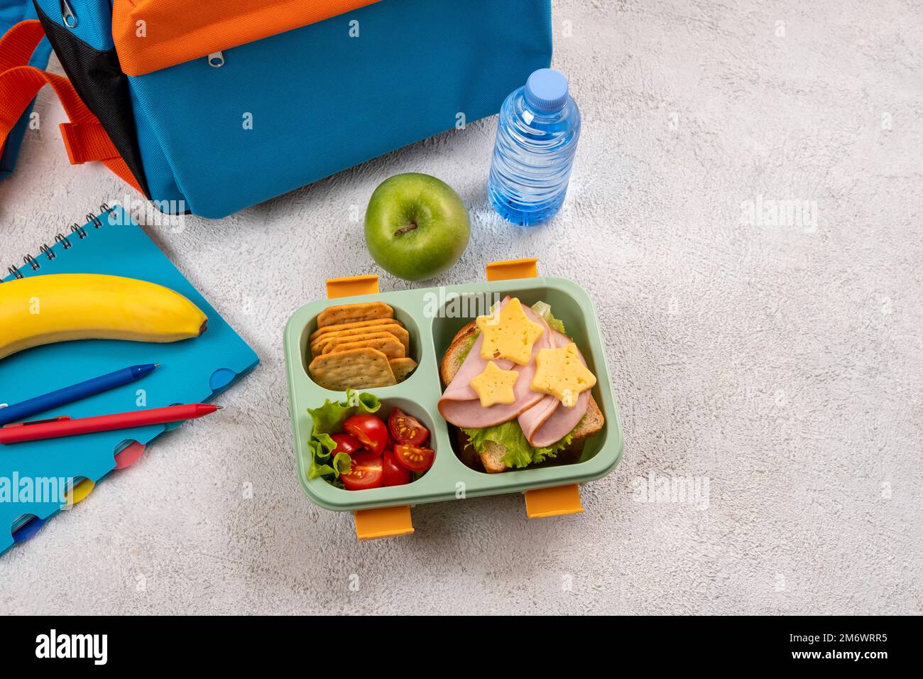 Pranzo al sacco a scuola sano con panino e insalata sul posto di lavoro vicino zaino. Forniture scolastiche, libri, mela e una bottiglia di w Foto Stock