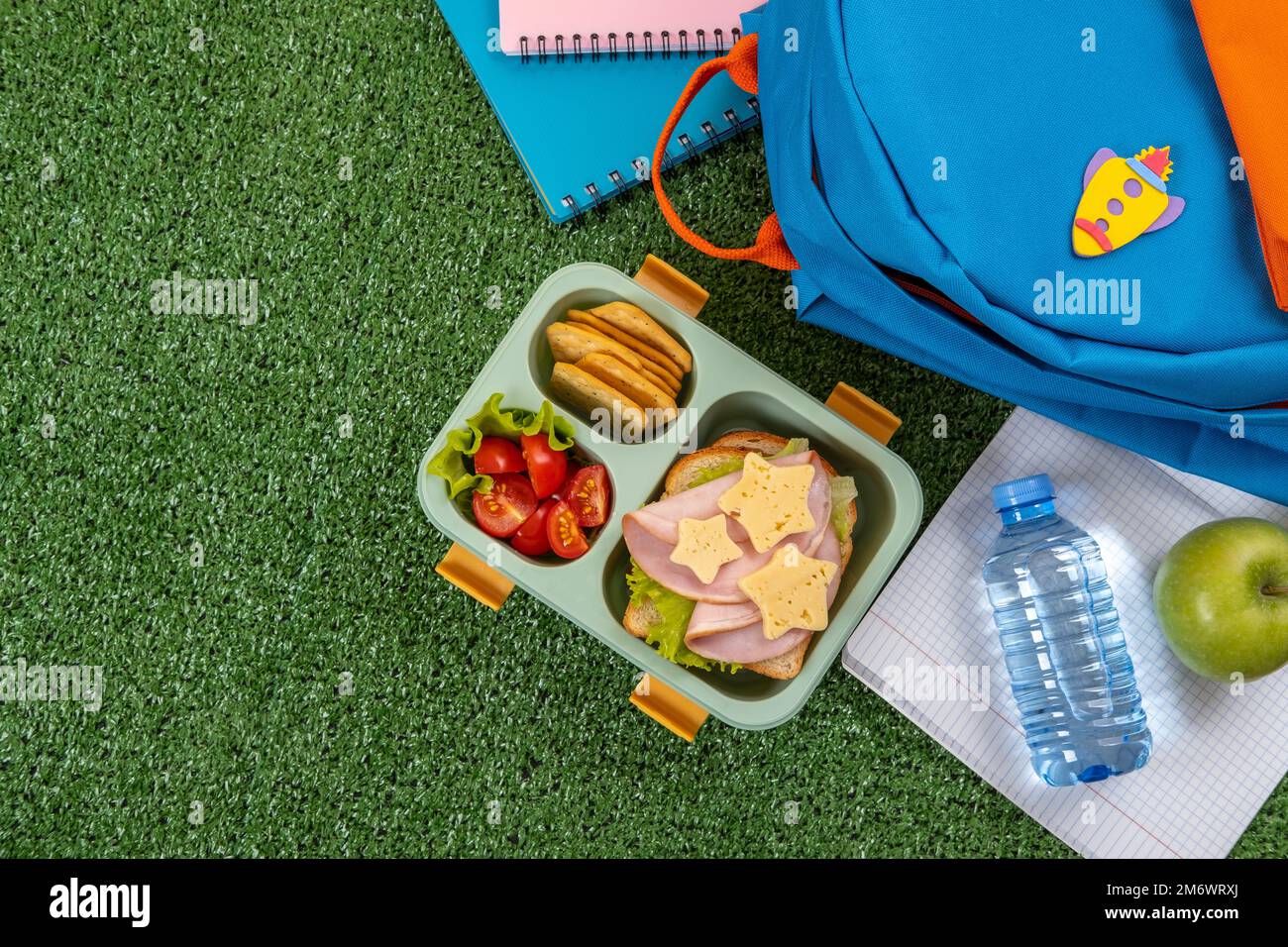 Pranzo al sacco a scuola sano con panino e insalata nel cortile della scuola. Forniture scolastiche, libri, mela e una bottiglia d'acqua. Torna a sc Foto Stock
