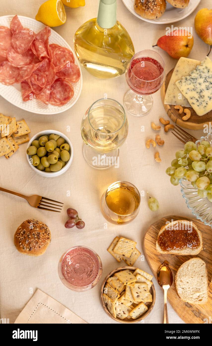 Calici e bottiglia di vino bianco con uva, formaggio e salumi su fondo tavolo chiaro. Vino bianco con formaggio e frutta. Wi Foto Stock