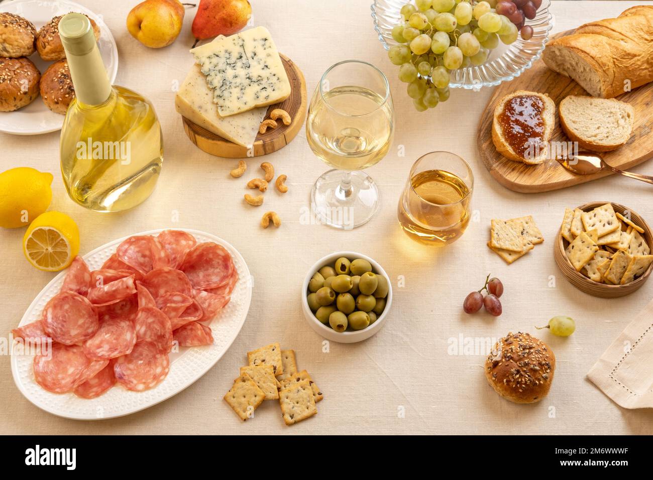 Calici e bottiglia di vino bianco con uva, formaggio e salumi su fondo tavolo chiaro. Vino bianco con formaggio e frutta. Wi Foto Stock