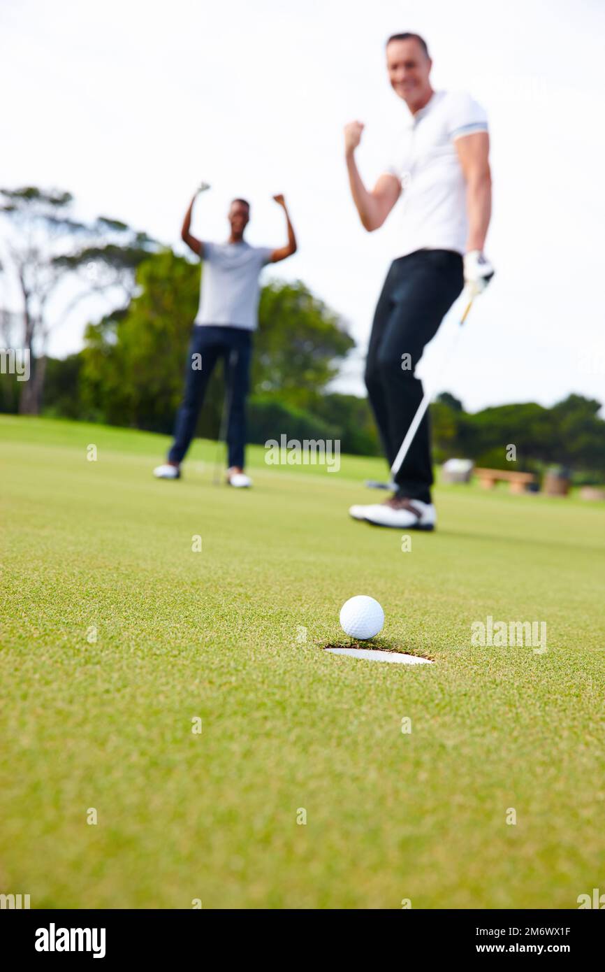 Il putt perfetto. Basso angolo colpo di una sfera di golf che si avvicina al foro mentre due golfers guardano sopra. Foto Stock