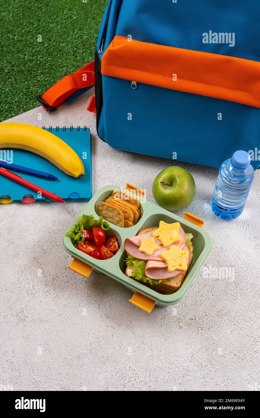 Pranzo al sacco a scuola sano con panino e insalata sul posto di lavoro vicino zaino. Forniture scolastiche, libri, mela e una bottiglia di w Foto Stock