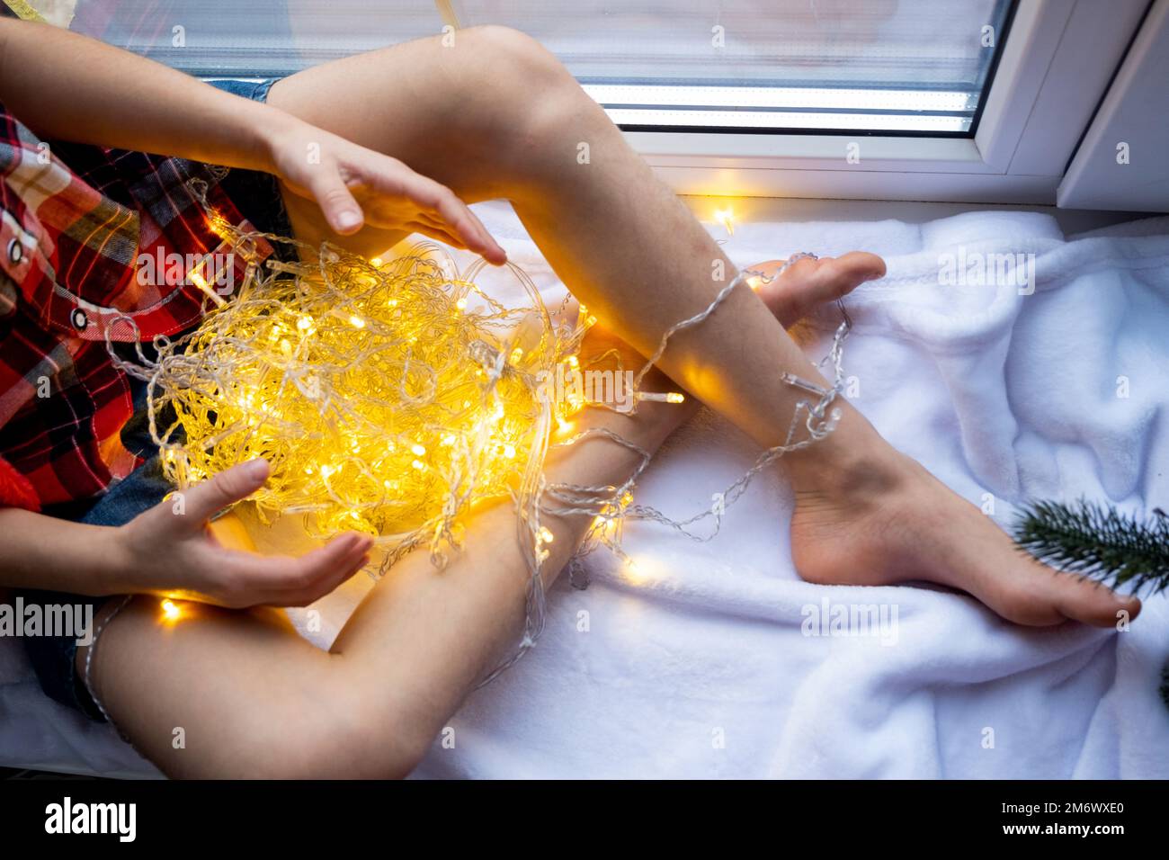 Una ragazza tiene in mano un ghirlone, seduta sul davanzale e sulle finestre, umore festivo, Natale, Capodanno Foto Stock