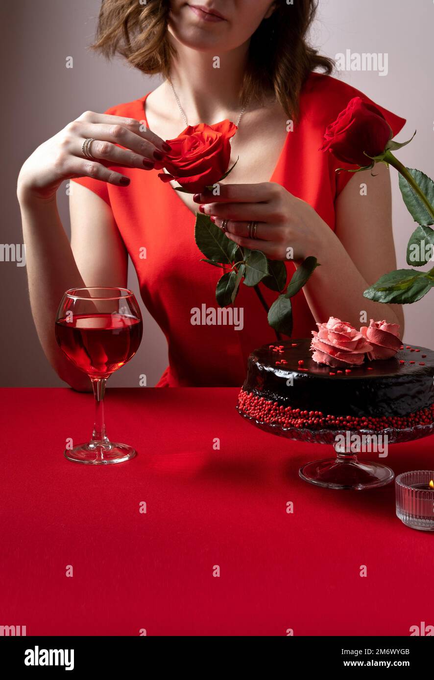 Donna in abito rosso con una mano che tiene una rosa rossa. Cena romantica a lume di candela. San Valentino. Impostazione tavolo festivo per San Valentino Foto Stock