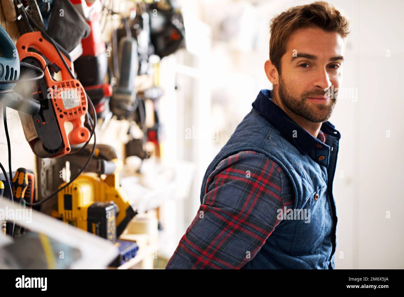 La mia officina, a modo mio. Ritratto di un bel giovane handyman in piedi davanti ai suoi utensili da lavoro. Foto Stock