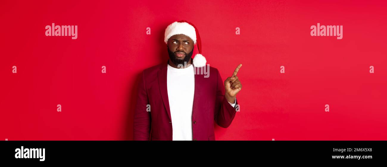 Natale, festa e concetto di festa. Scettico e cupo afro-americano uomo puntando il dito a sinistra, guardando deluso, sta Foto Stock