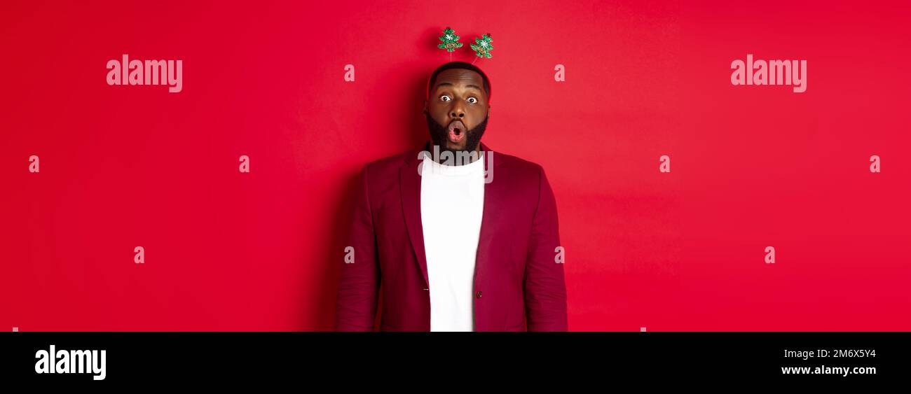 Buon Natale. Felice uomo afroamericano celebrando il nuovo anno, indossando la fascia della festa e facendo i volti divertenti, in piedi sopra Foto Stock
