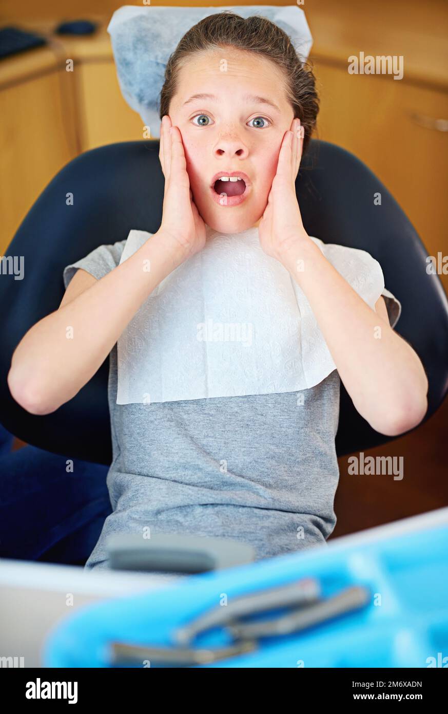 Nel sedile caldo. Una ragazza giovane che guarda terrorizzata mentre si siede in una sedia dentista. Foto Stock