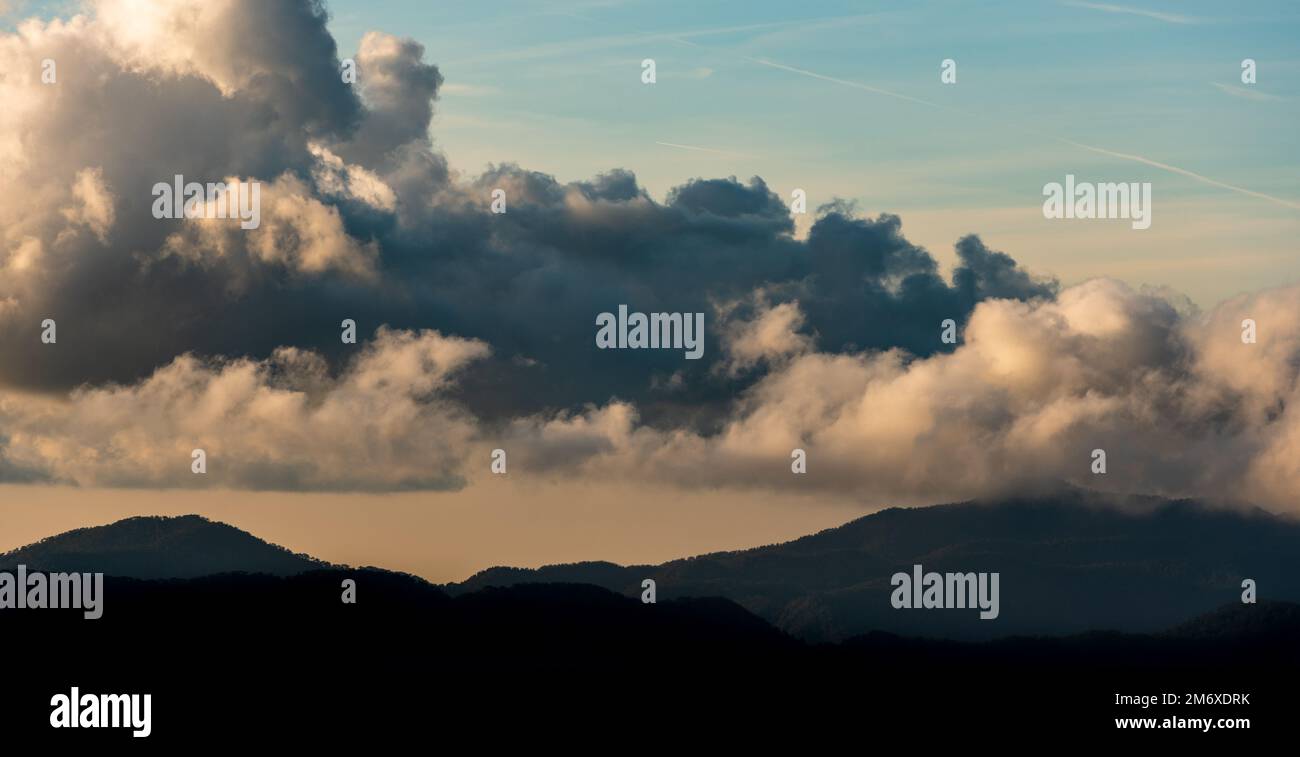 Silhouette di cime montane con nebbia e nuvole drammatiche. Tramonto colorato. Foto Stock